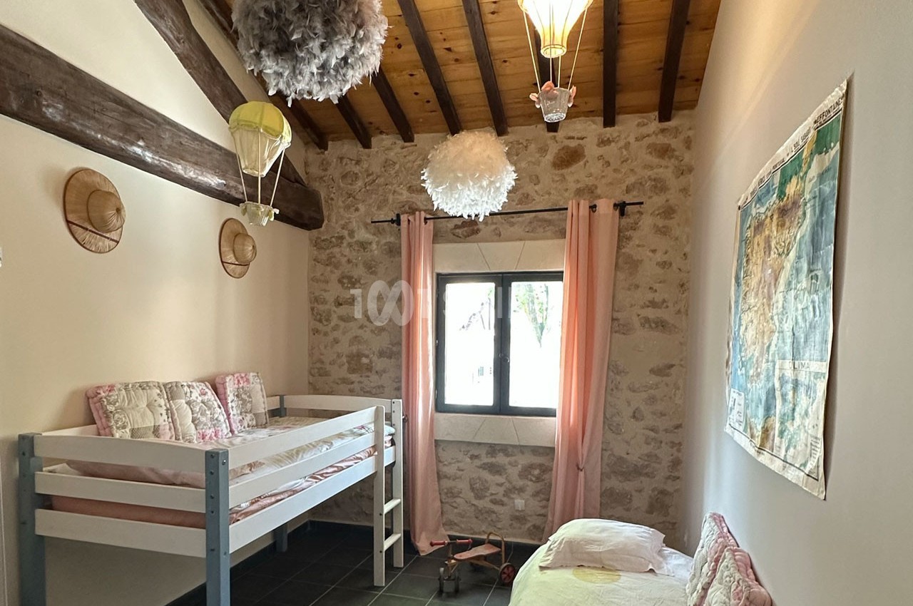 Chambre avec lits superposés, murs en pierre, plafond en bois, décorations aériennes et lumière naturelle.