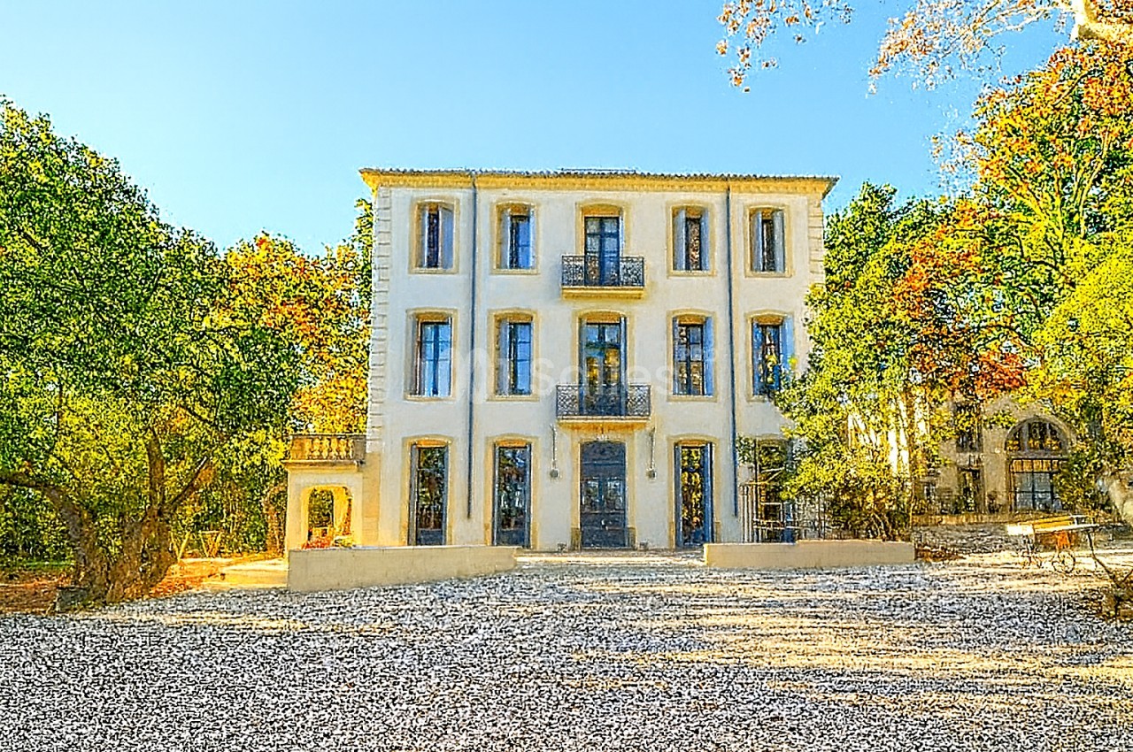 Façade d'un bâtiment ancien à trois étages entouré d'arbres, avec une cour en gravier au premier plan.