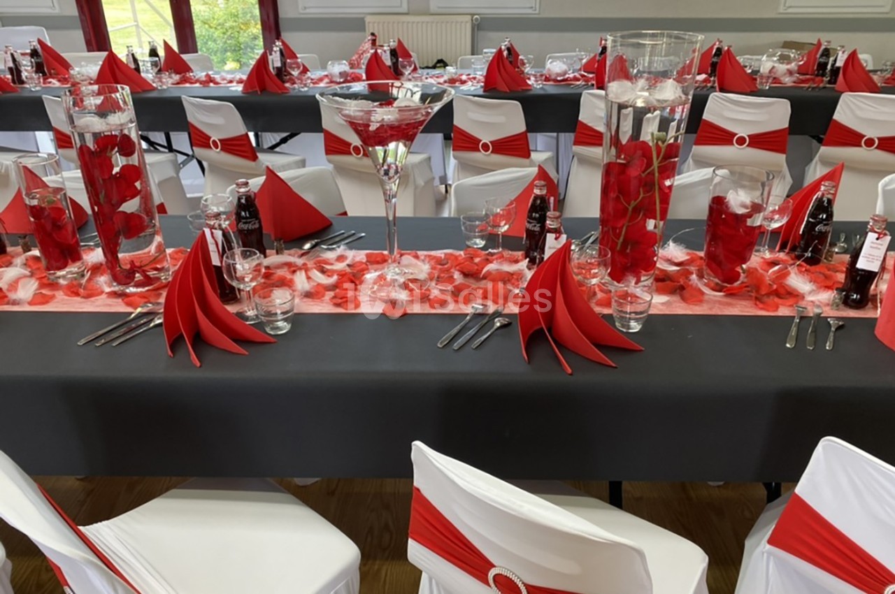 Salle décorée pour un événement avec tables noires, nappes rouges et blanches, pétales et centres de table fleuris.