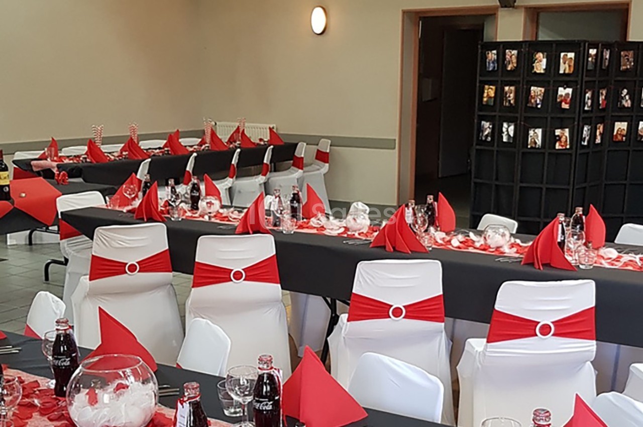 Salle décorée pour un événement avec des tables dressées en noir, rouge et blanc, et des chaises assorties.