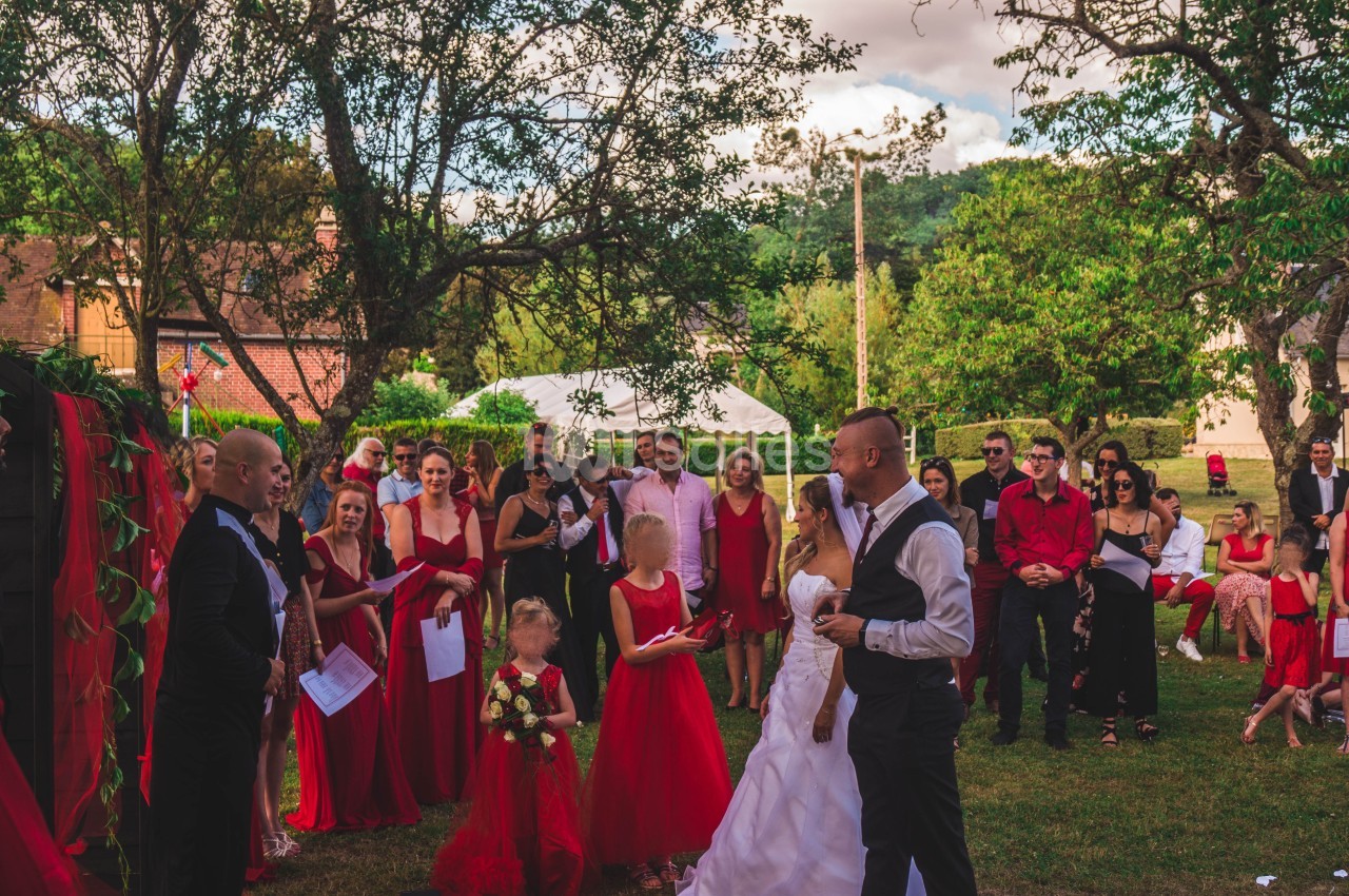 Cérémonie de mariage en extérieur avec des invités vêtus de rouge et de noir, entourés de verdure et de décorations.