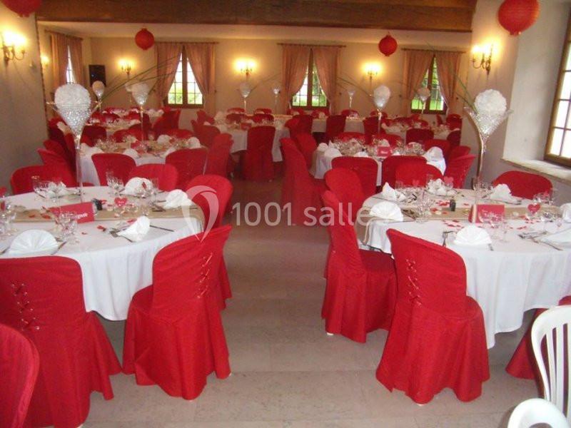 Salle de réception décorée avec des nappes blanches, des housses de chaise rouges et des centres de table élégants.
