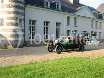 Voiture ancienne verte stationnée devant un bâtiment en pierre blanche avec des fenêtres à croisillons.