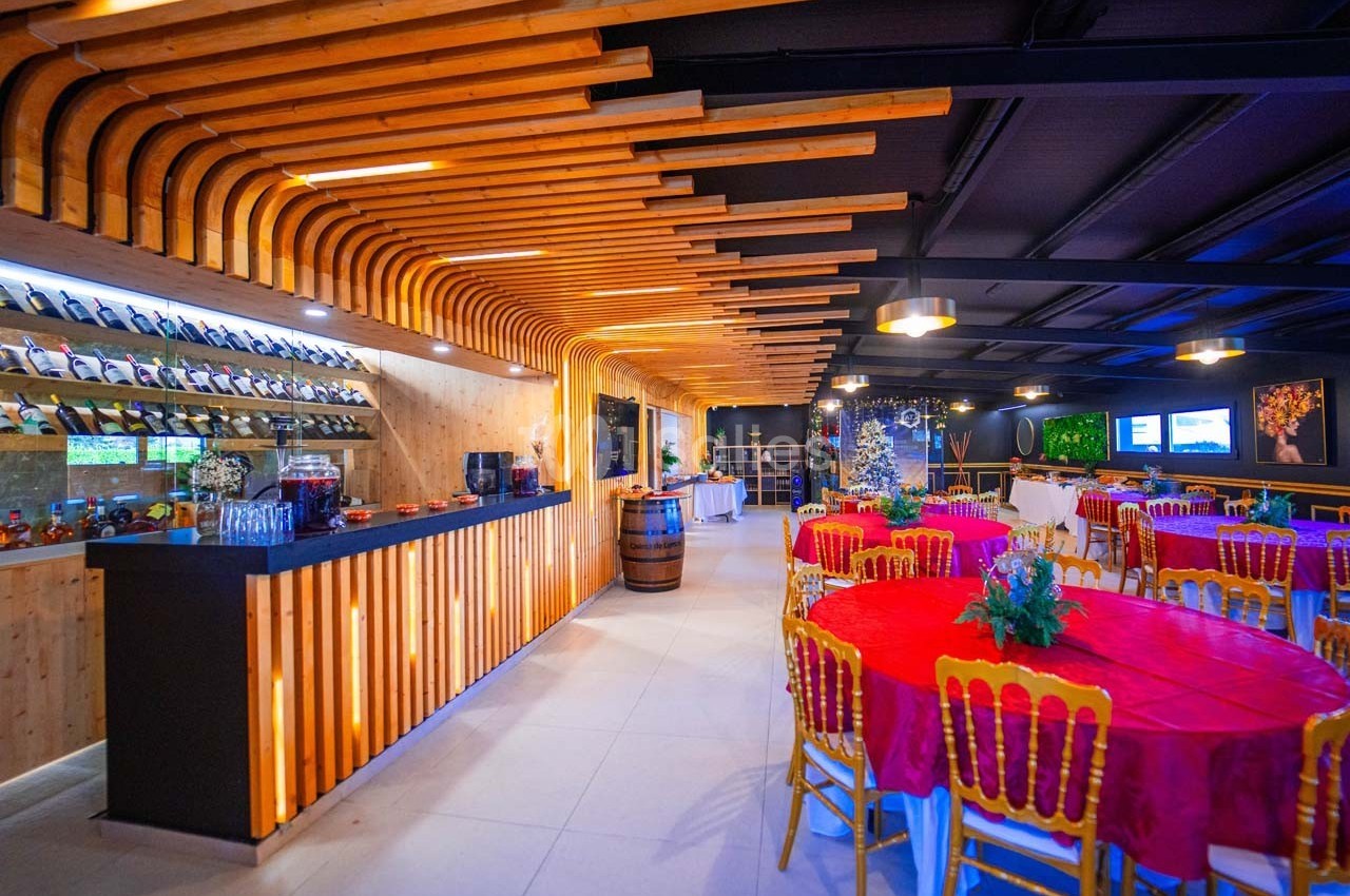 Salle de réception avec tables rondes habillées de nappes rouges, bar en bois et décoration lumineuse moderne.