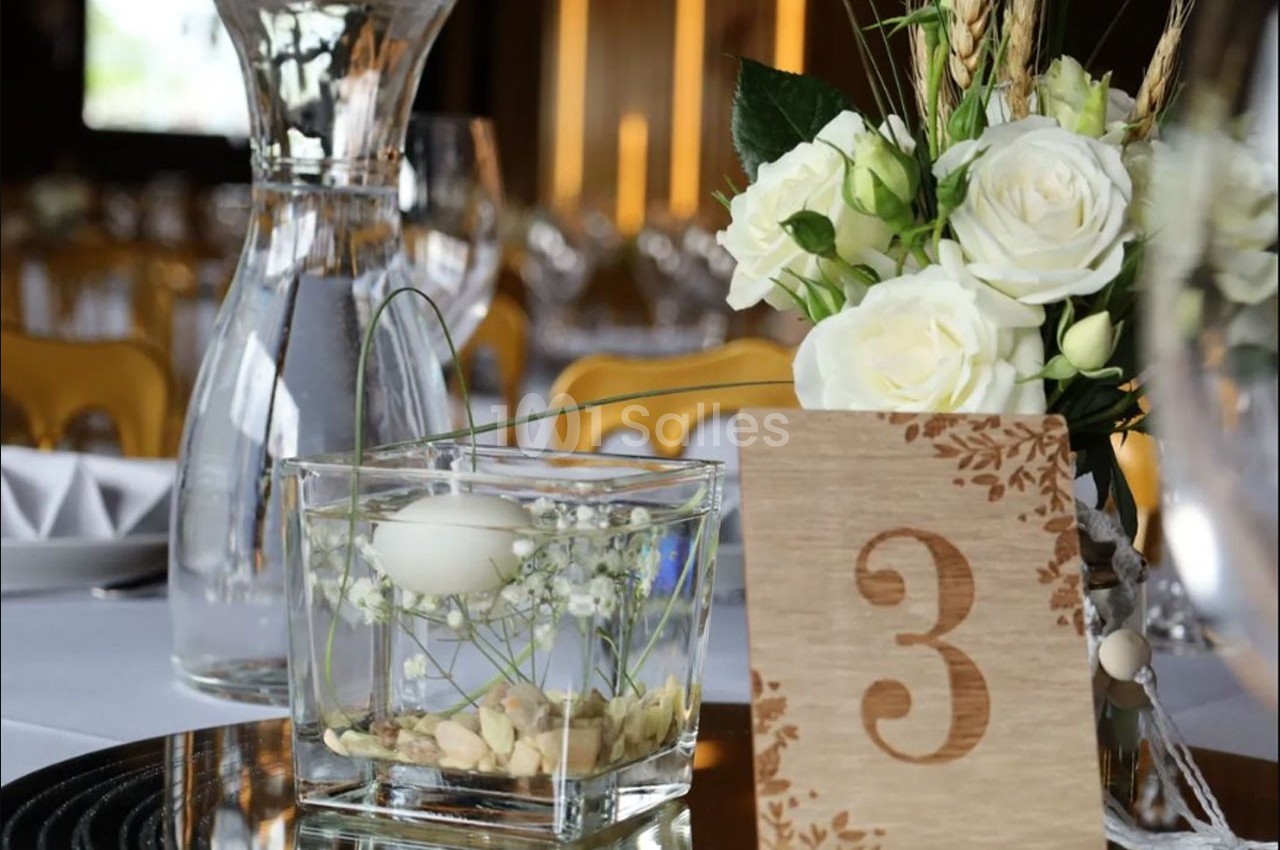 Centre de table avec une carafe d'eau, un vase contenant une fleur et un œuf flottant, un bouquet et un panneau numéro 3.