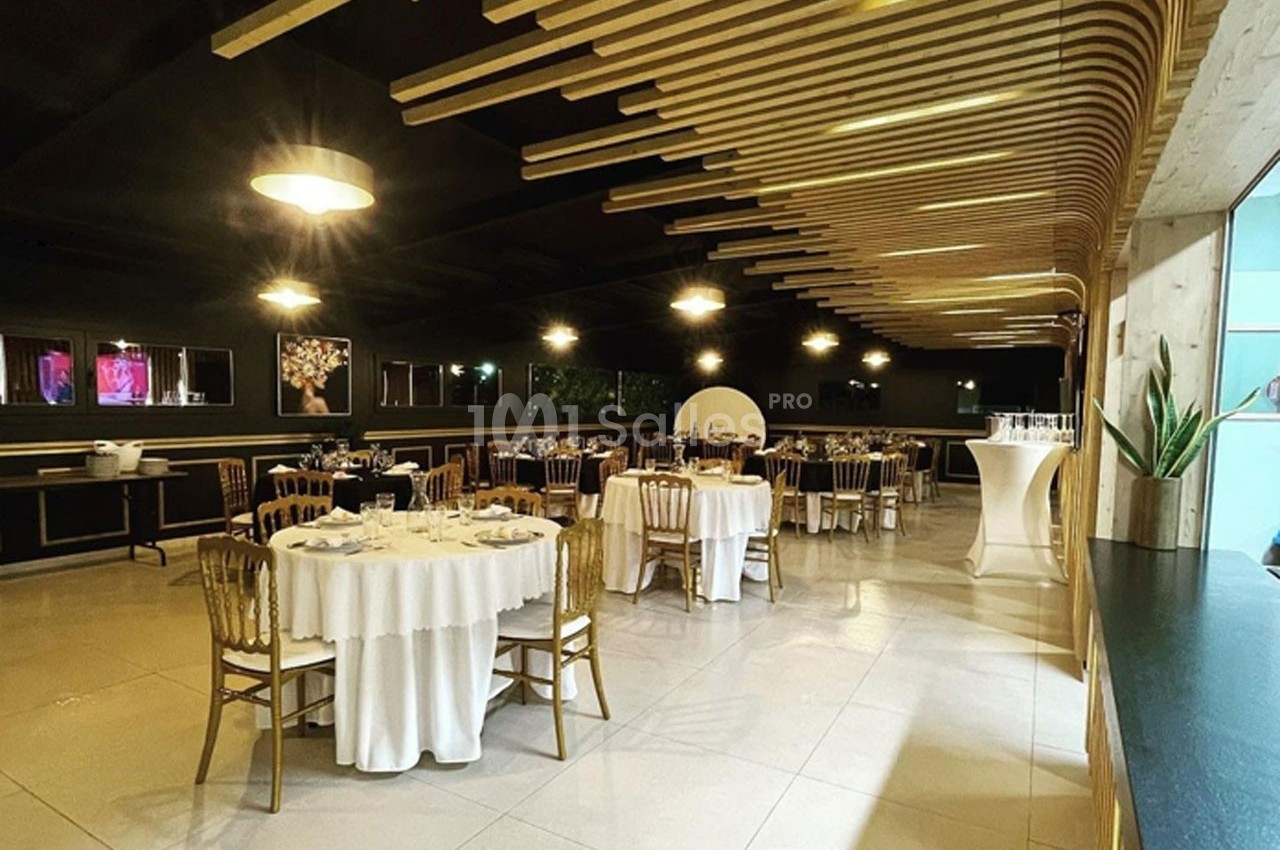 Salle de réception élégante avec tables rondes dressées, chaises dorées et éclairage chaleureux.