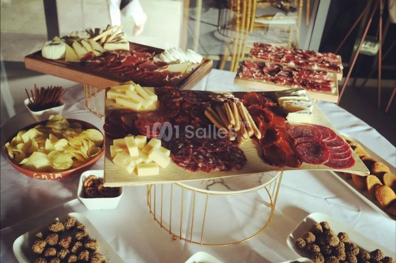 Plateaux de charcuterie et fromages variés entourés de bols de chips, fruits secs et autres accompagnements sur une table.