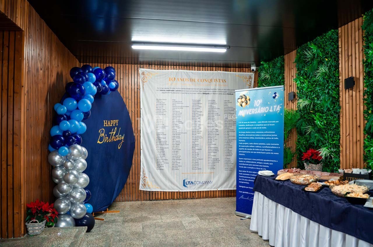 Décoration d'anniversaire avec ballons bleus, table de buffet garnie et panneaux d'information dans une salle en bois.