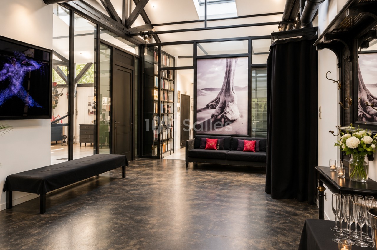 Espace intérieur moderne avec sol en bois sombre, canapés noirs, grandes photos murales et décoration élégante.