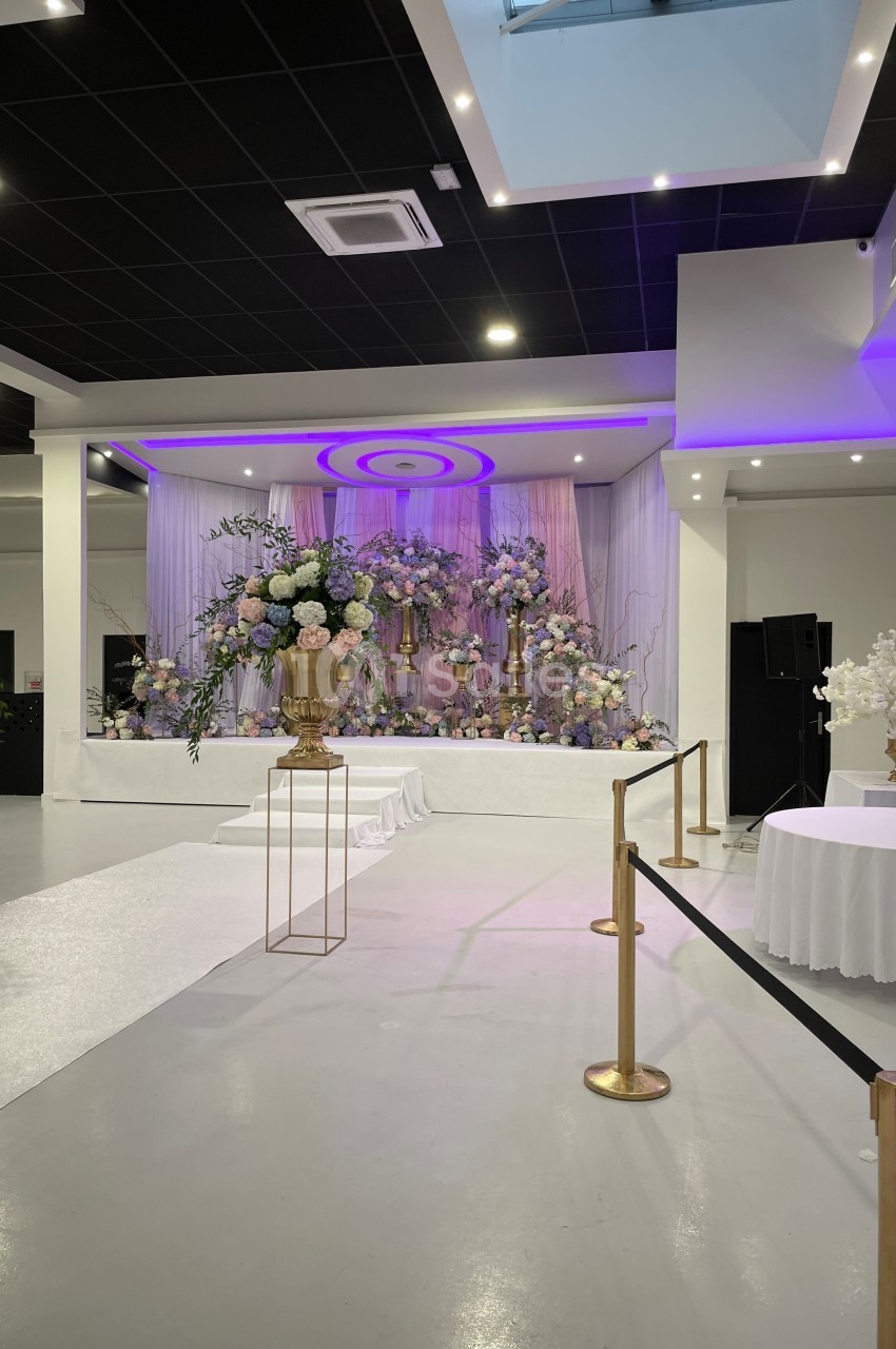 Décoration florale élégante avec des fleurs pastel sur une scène dans une salle de réception moderne et lumineuse.