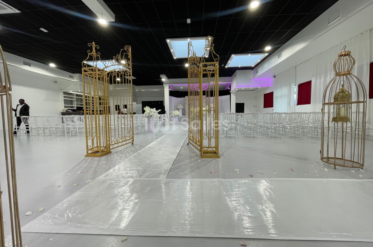 Allée centrale décorée de cages dorées dans une salle de réception avec chaises blanches et éclairage tamisé.