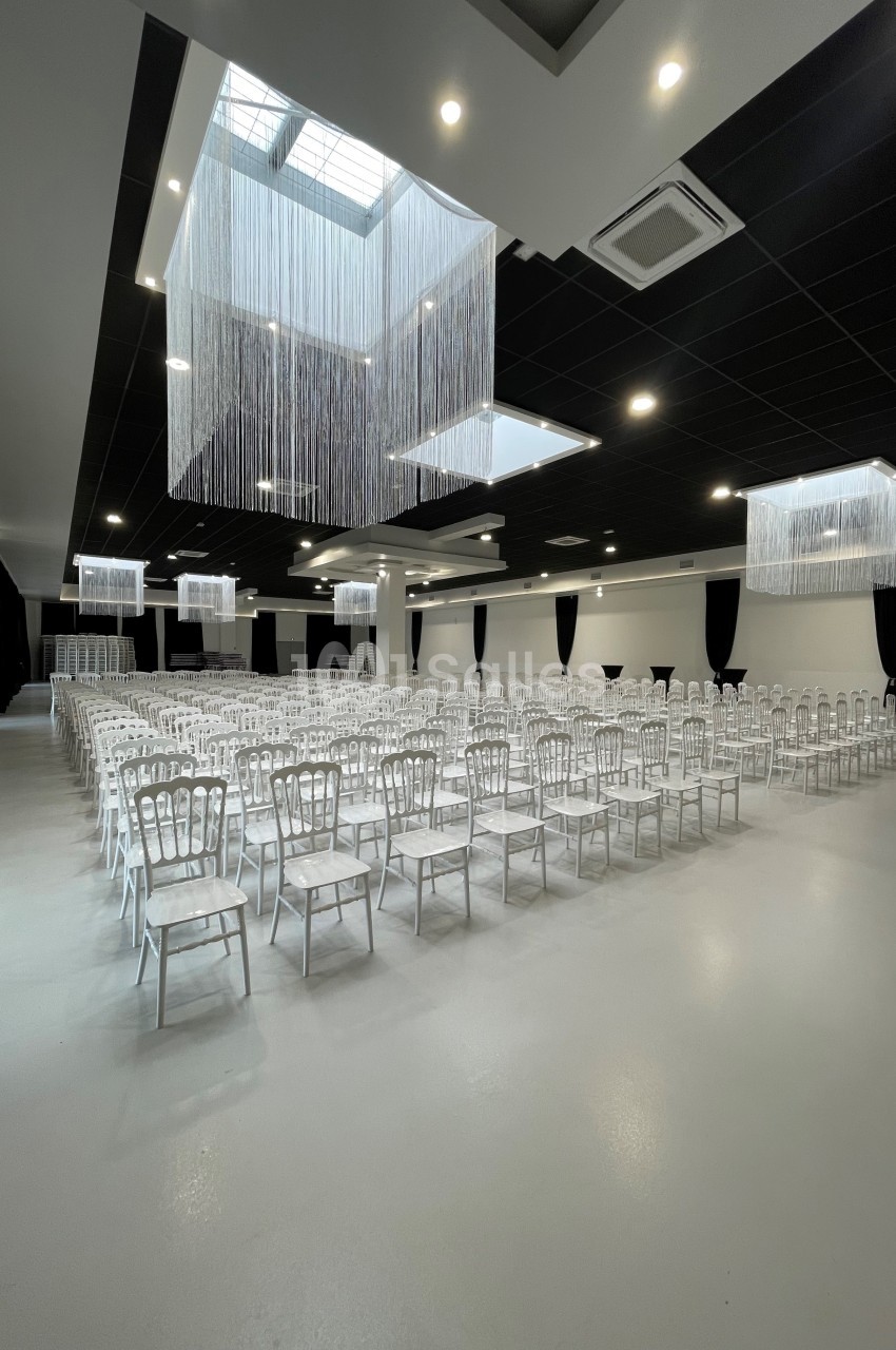 Salle de réception spacieuse avec rangées de chaises blanches alignées sous des lustres modernes suspendus.