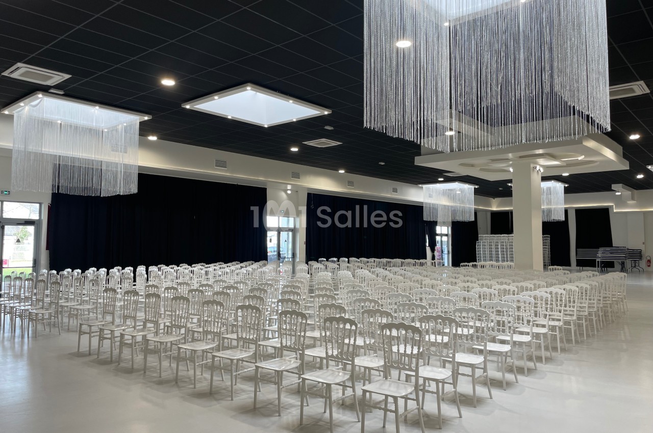 Salle de réception avec des rangées de chaises blanches alignées sous un plafond décoré de fils suspendus.