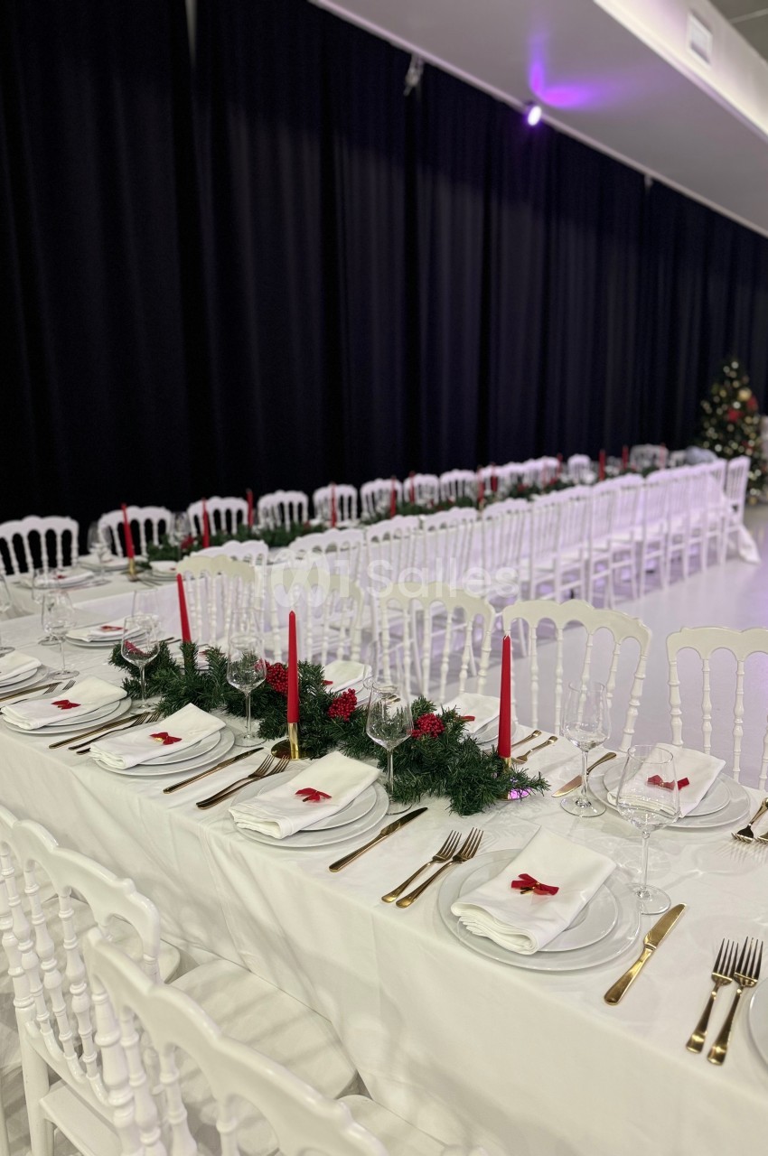 Tables de réception décorées avec nappes blanches, bougies rouges, couverts dorés et guirlandes vertes.