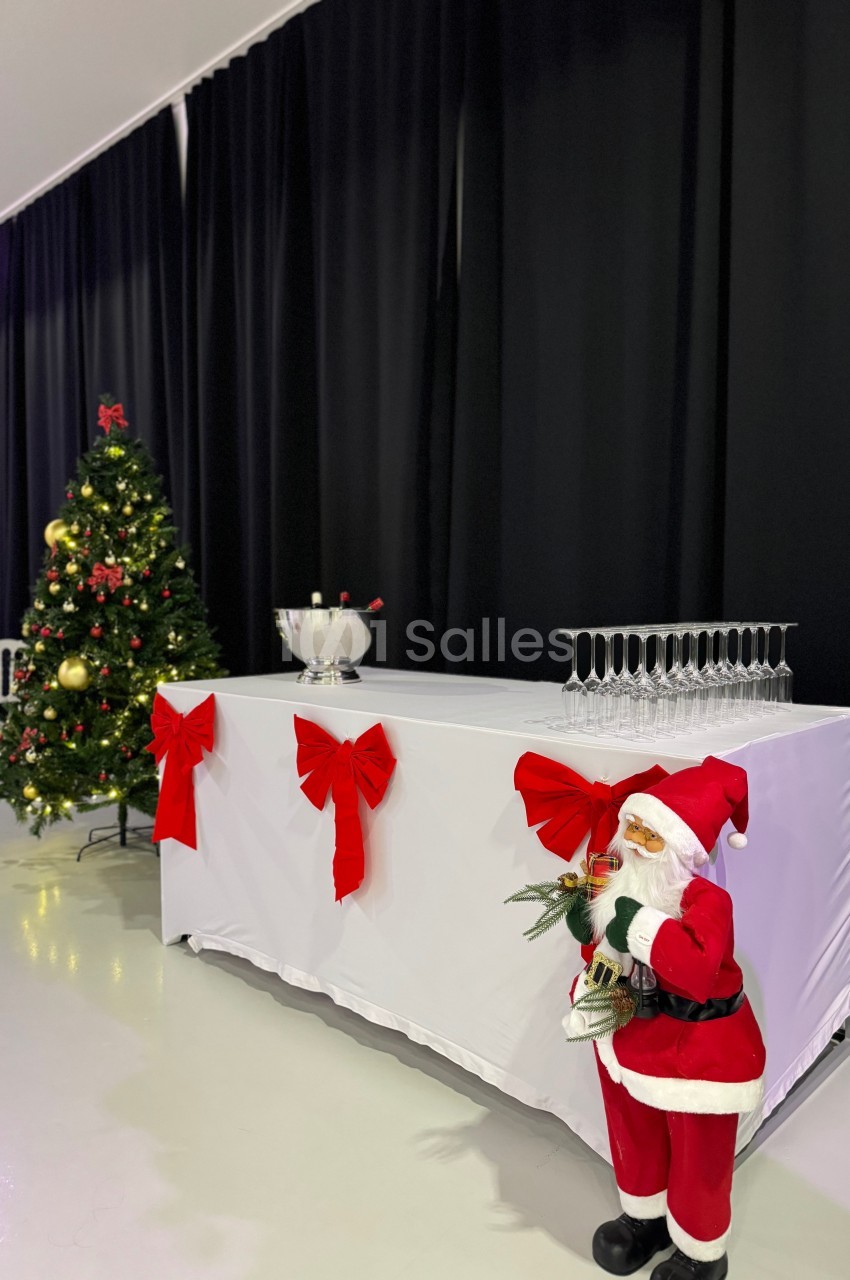 Table décorée avec des rubans rouges, un Père Noël miniature, un sapin de Noël illuminé et des flûtes à champagne.