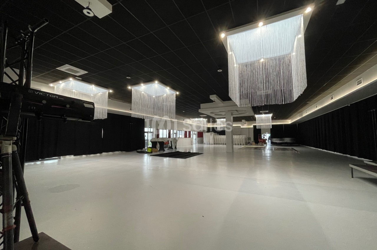 Salle spacieuse avec sol clair, plafond noir, rideaux sombres et lustres modernes suspendus.
