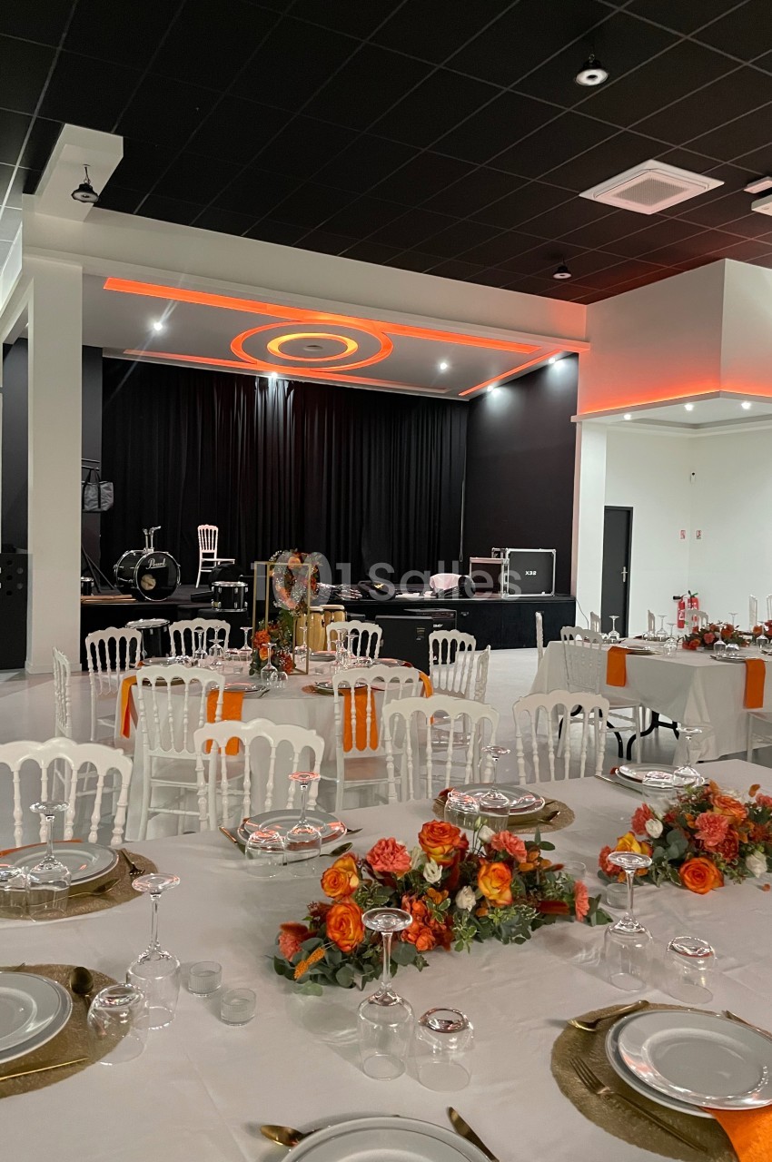 Salle de réception décorée avec des tables dressées, des chaises blanches et des arrangements floraux orange devant une…