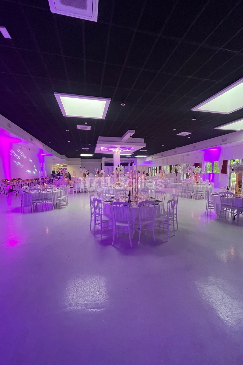 Salle de réception spacieuse avec tables rondes décorées, éclairage violet et plafond noir avec lumières intégrées.