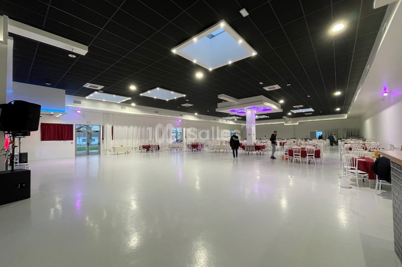 Salle spacieuse avec sol brillant, tables dressées et éclairage moderne, quelques personnes en arrière-plan.