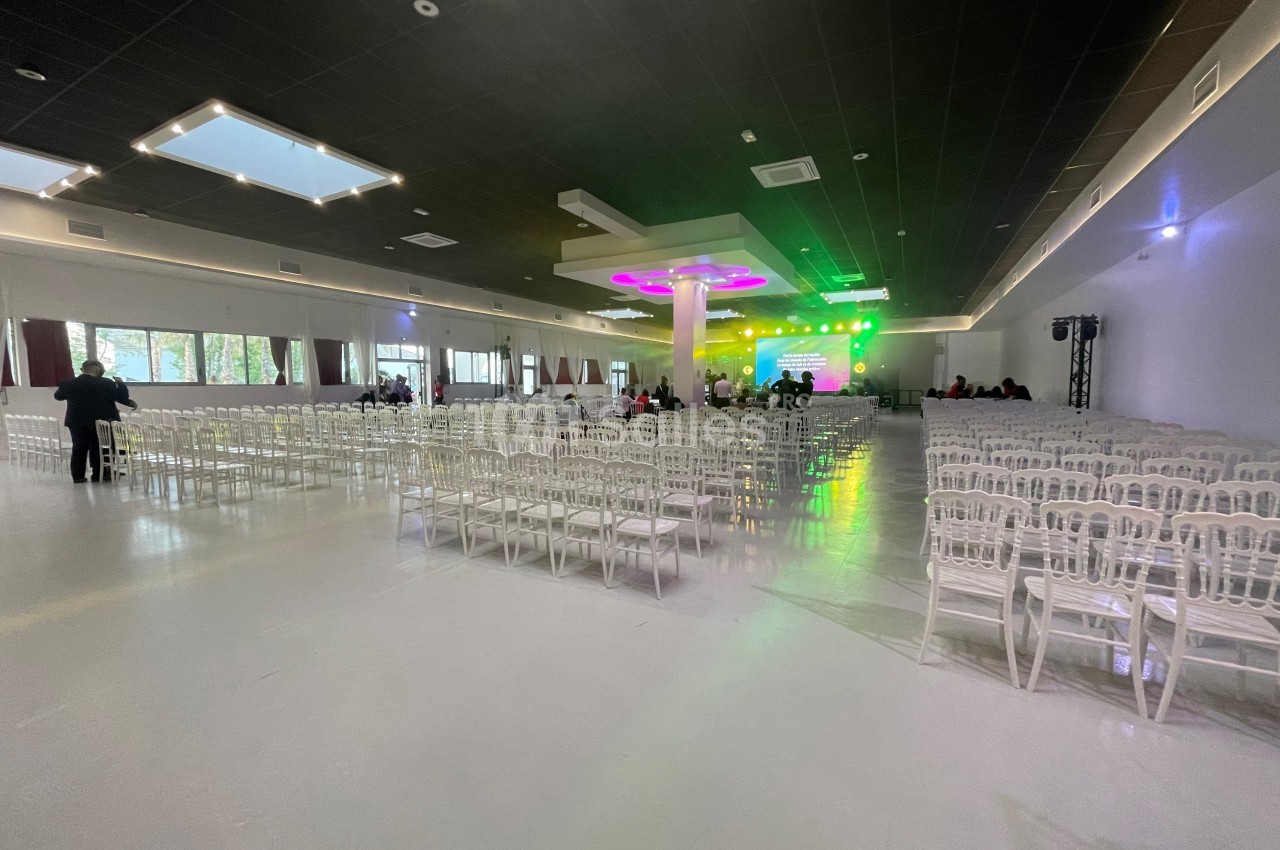Salle spacieuse avec des rangées de chaises blanches, éclairage coloré sur une scène au fond.