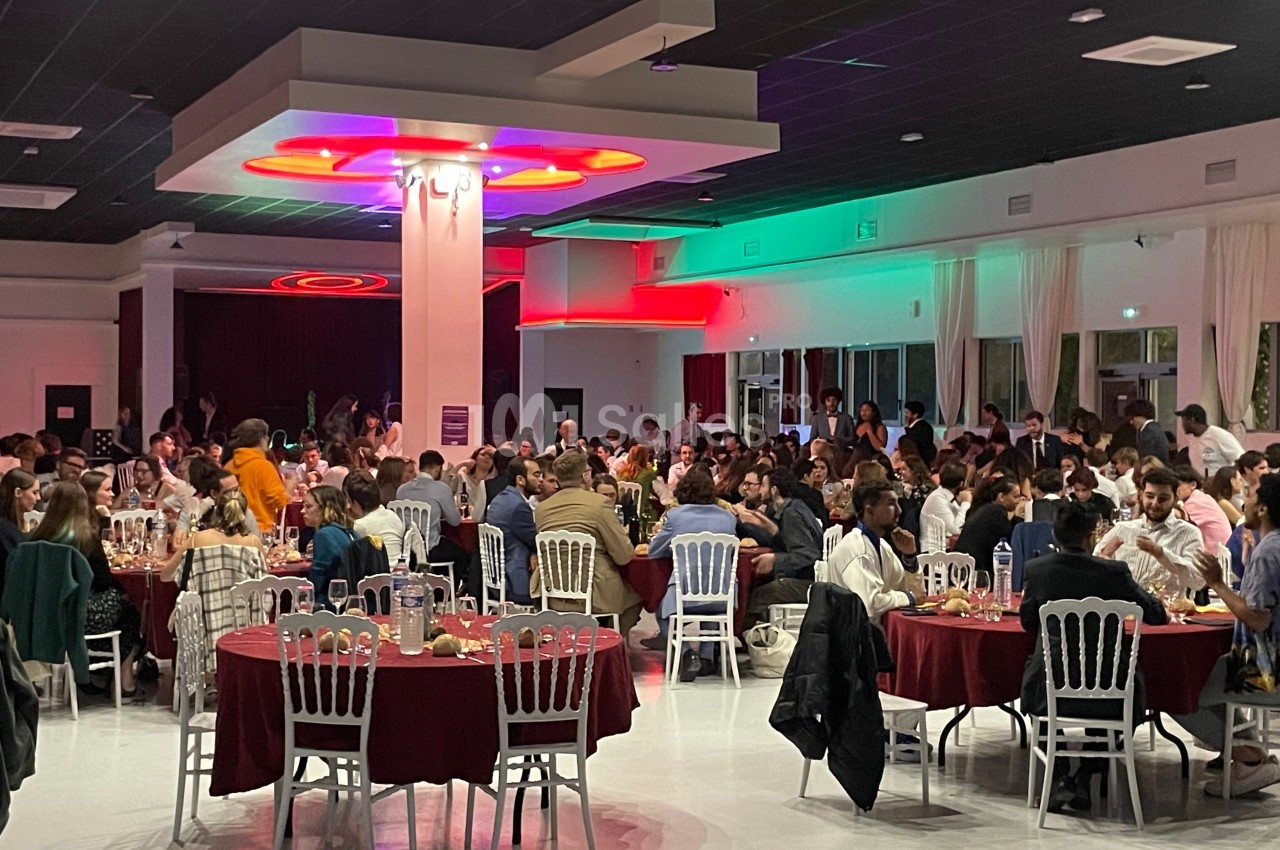 Salle remplie de personnes assises à des tables rondes, lors d'un événement ou d'un repas collectif.
