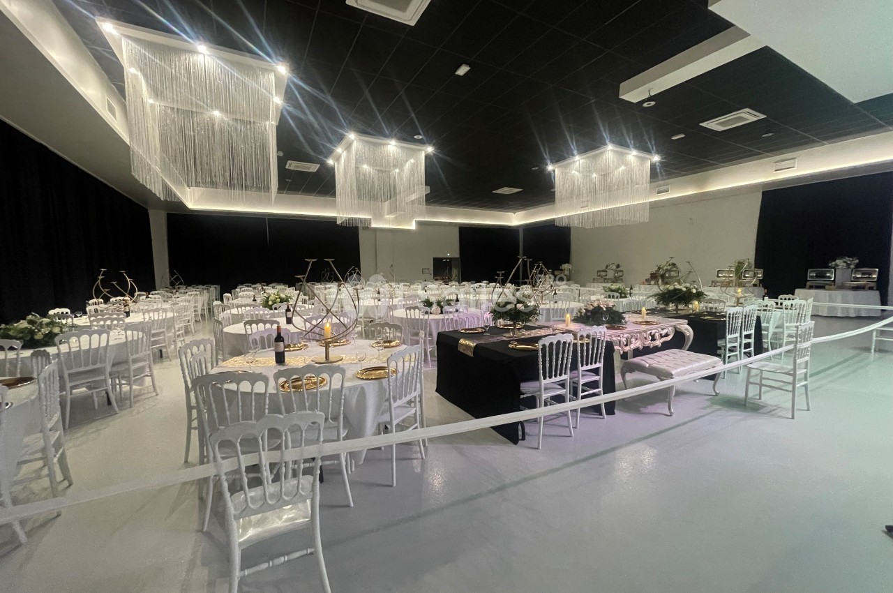 Salle de réception décorée avec des tables rondes, nappes blanches, chaises élégantes et éclairage suspendu moderne.