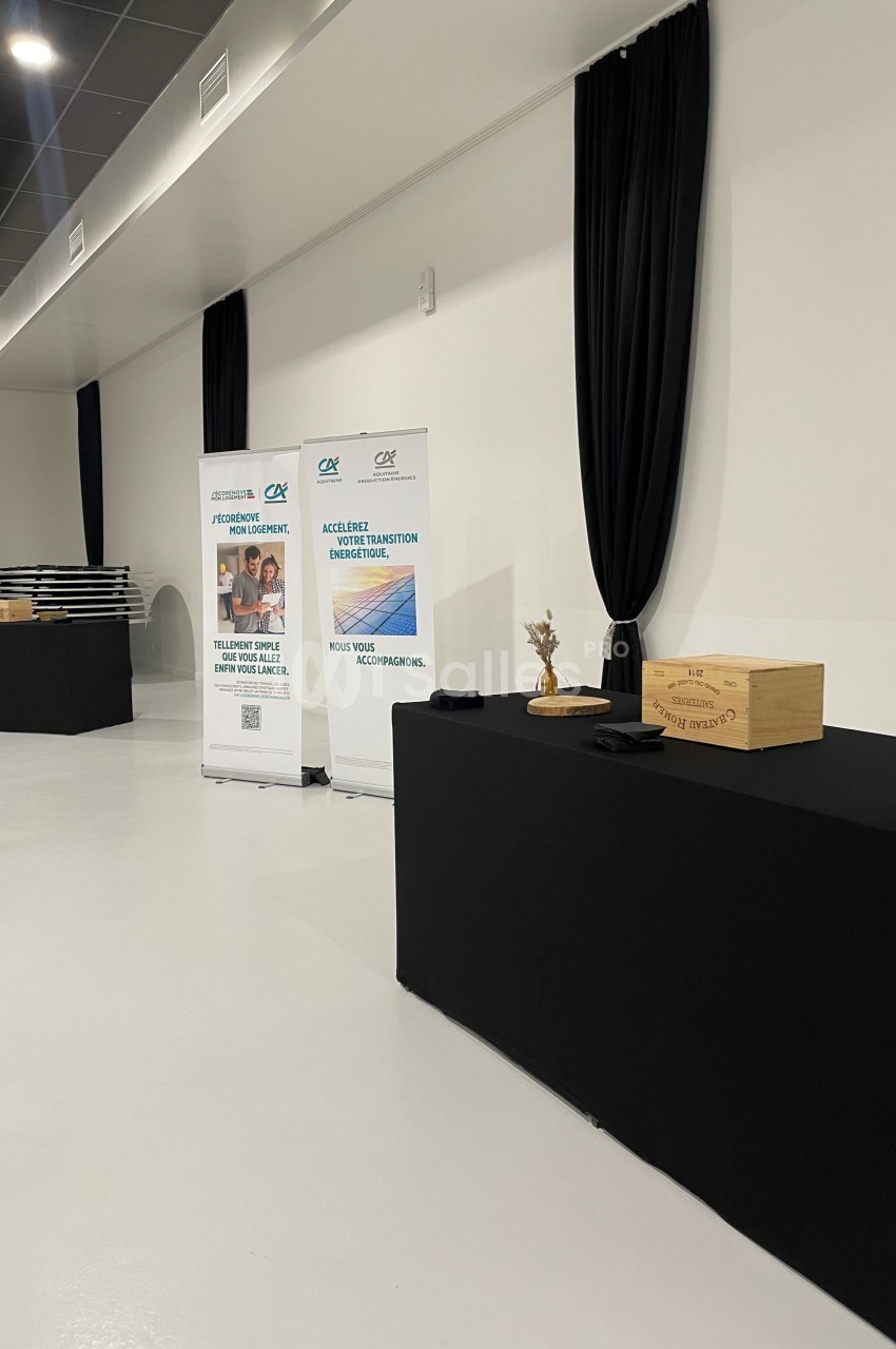 Deux roll-ups promotionnels et une table noire avec des boîtes en bois dans une salle lumineuse au sol blanc.