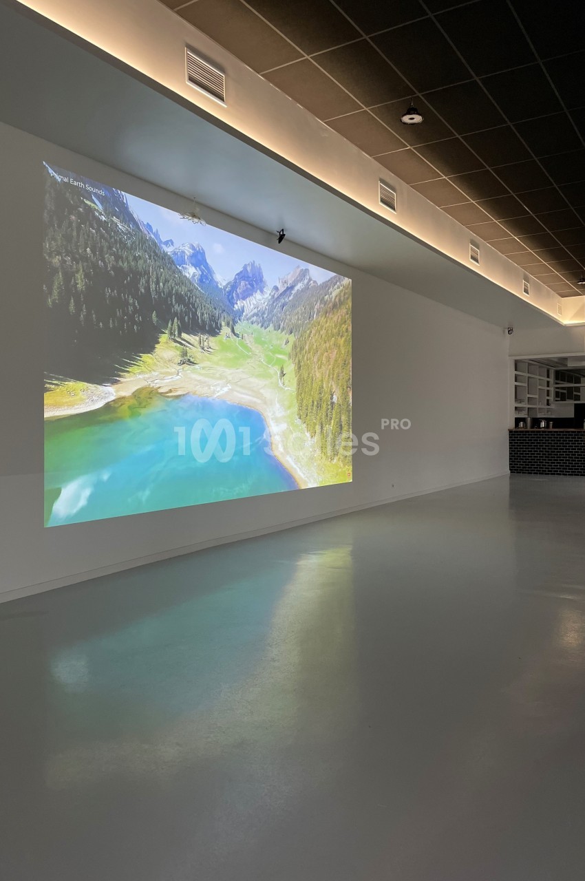 Projection d'un paysage de montagne avec lac turquoise sur un mur blanc dans une pièce moderne et épurée.