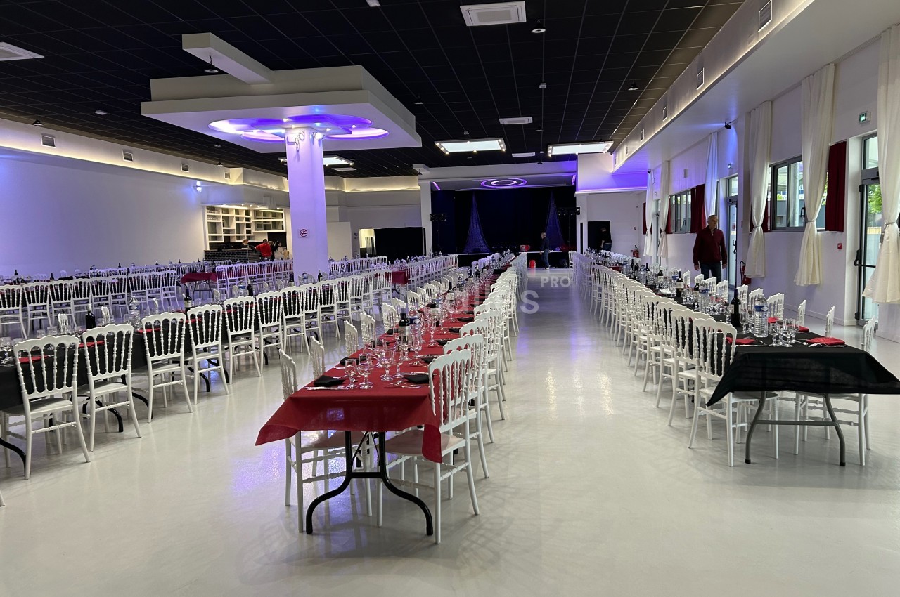 Grande salle de réception avec tables alignées, nappes rouges et noires, chaises blanches et éclairage moderne.