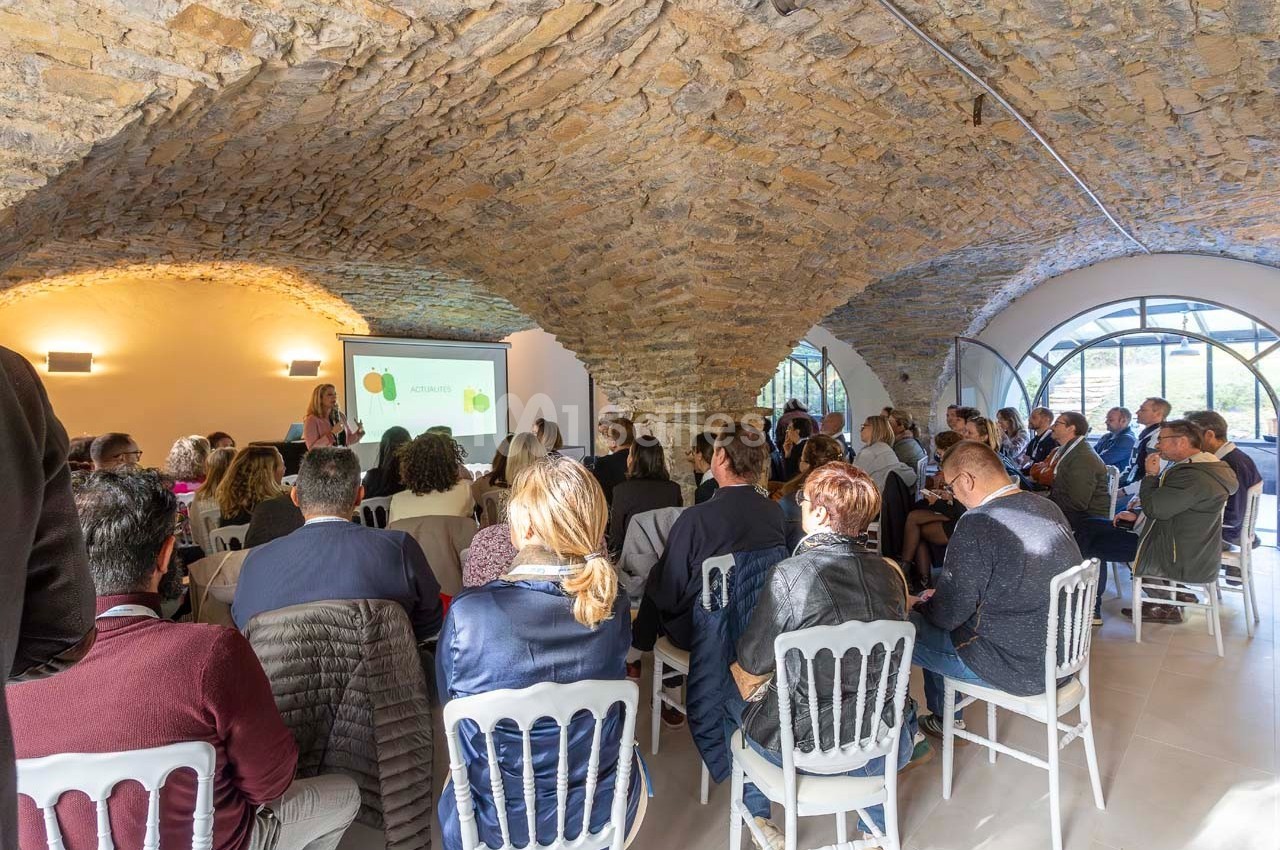 Un groupe de personnes assiste à une présentation dans une salle voûtée en pierre avec un écran de projection.