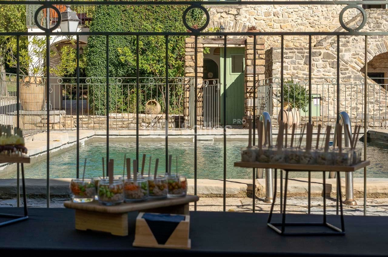 Buffet en extérieur avec verrines disposées sur une table, en arrière-plan une piscine et un bâtiment en pierre.