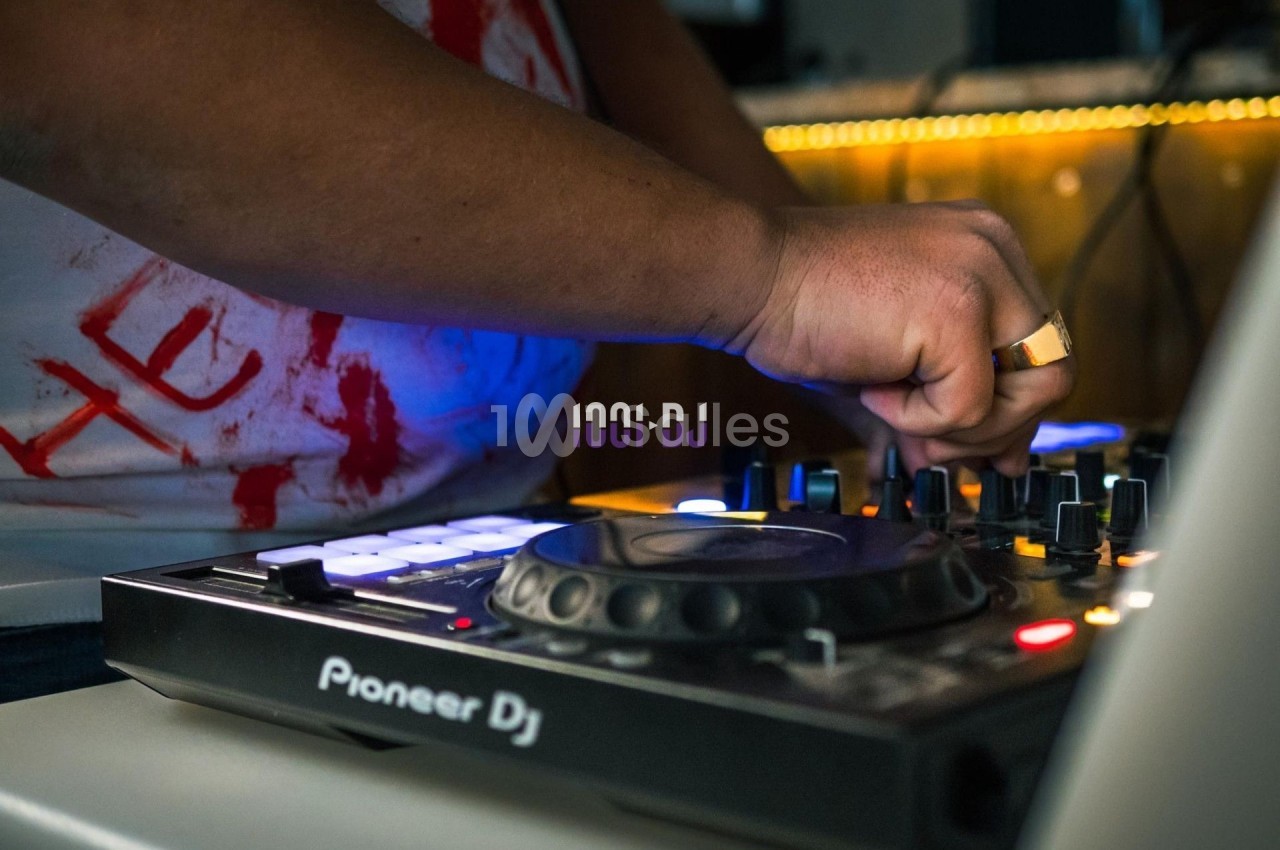 Un DJ ajuste les commandes d'une table de mixage Pioneer dans un environnement faiblement éclairé.