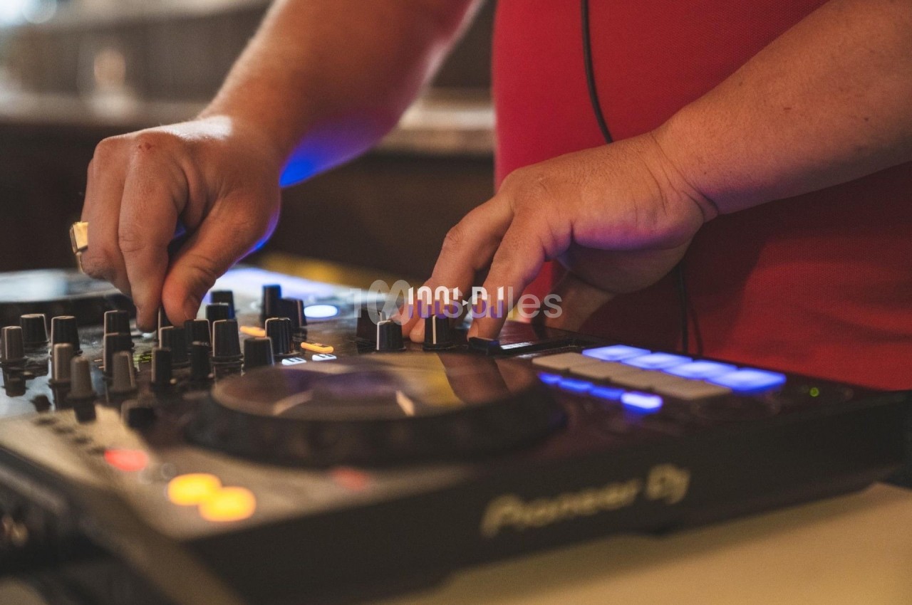 Mains manipulant une table de mixage DJ avec des boutons et des lumières colorées.
