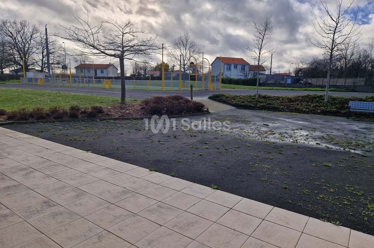 Allée pavée donnant sur un espace extérieur avec terrain de sport, pelouse, arbres et maisons en arrière-plan.