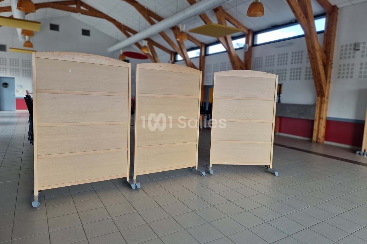 Trois panneaux en bois sur roulettes disposés dans une grande salle lumineuse avec charpente apparente.