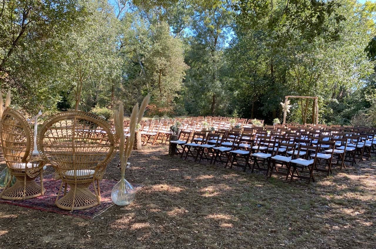 Chaises en bois alignées pour une cérémonie en plein air, avec des fauteuils en rotin et une arche décorative sous les…