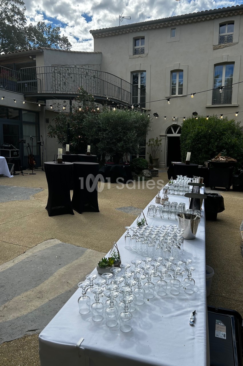 Table dressée avec des verres et des seaux à glace dans une cour extérieure, entourée de bâtiments et d'arbres.