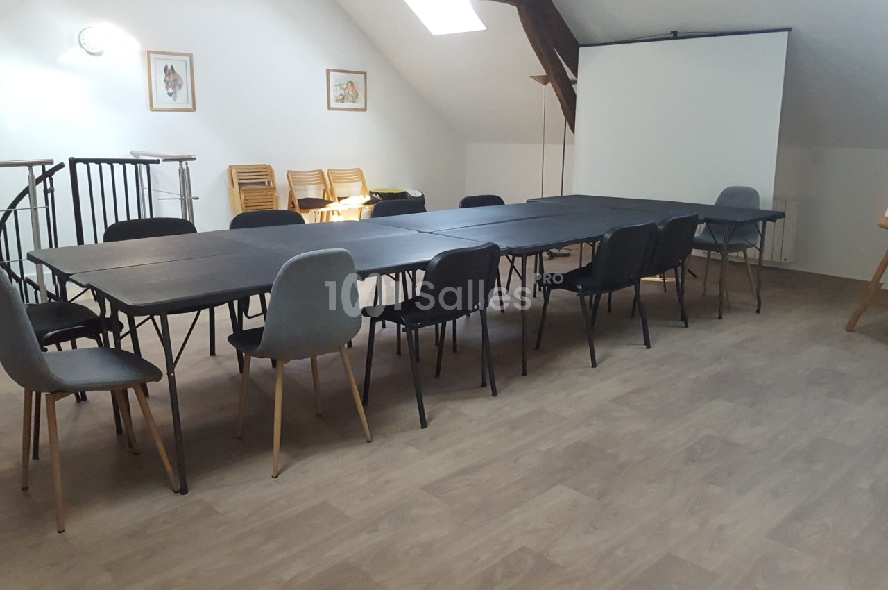 Salle de réunion lumineuse avec tables noires alignées, chaises variées, tableau blanc et écran de projection.