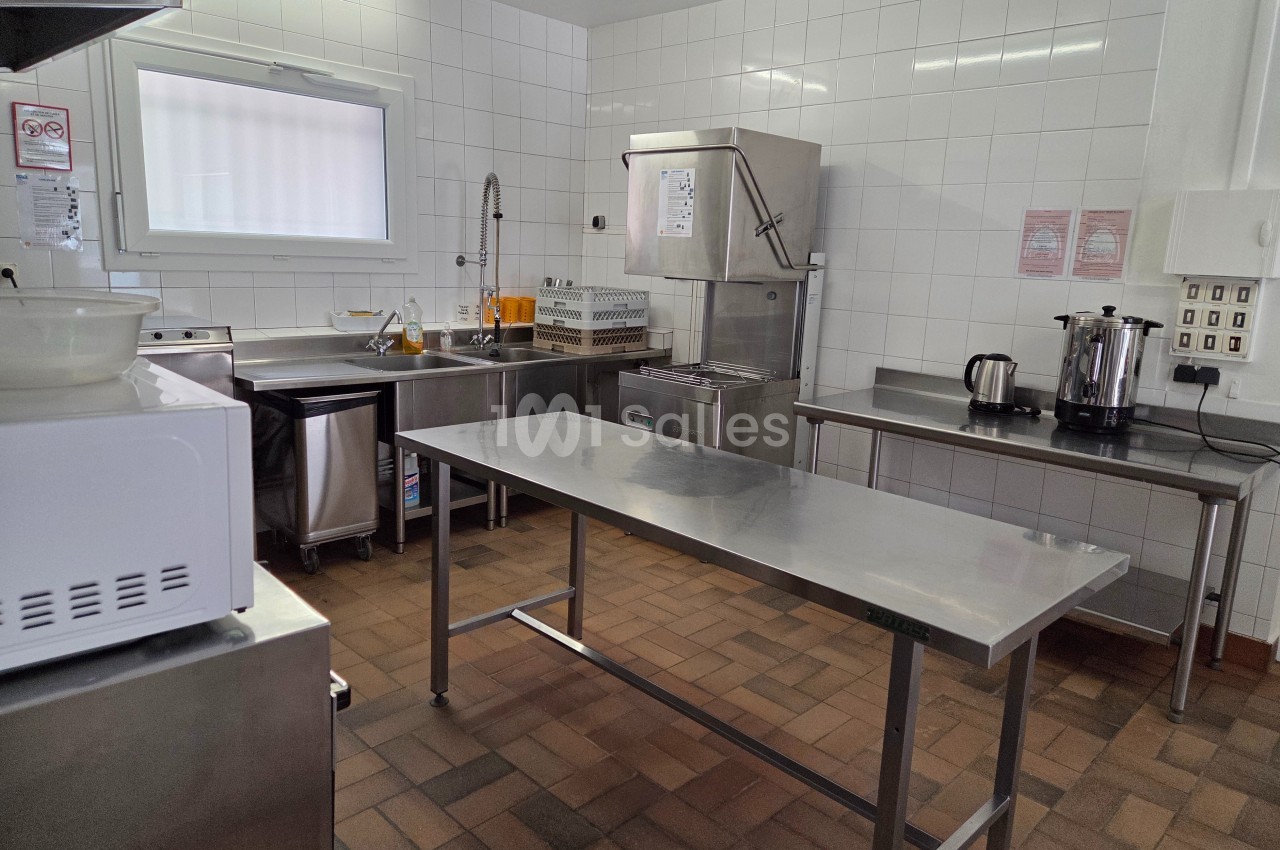 Cuisine professionnelle avec plan de travail en inox, évier, lave-vaisselle industriel et équipements électroménagers.