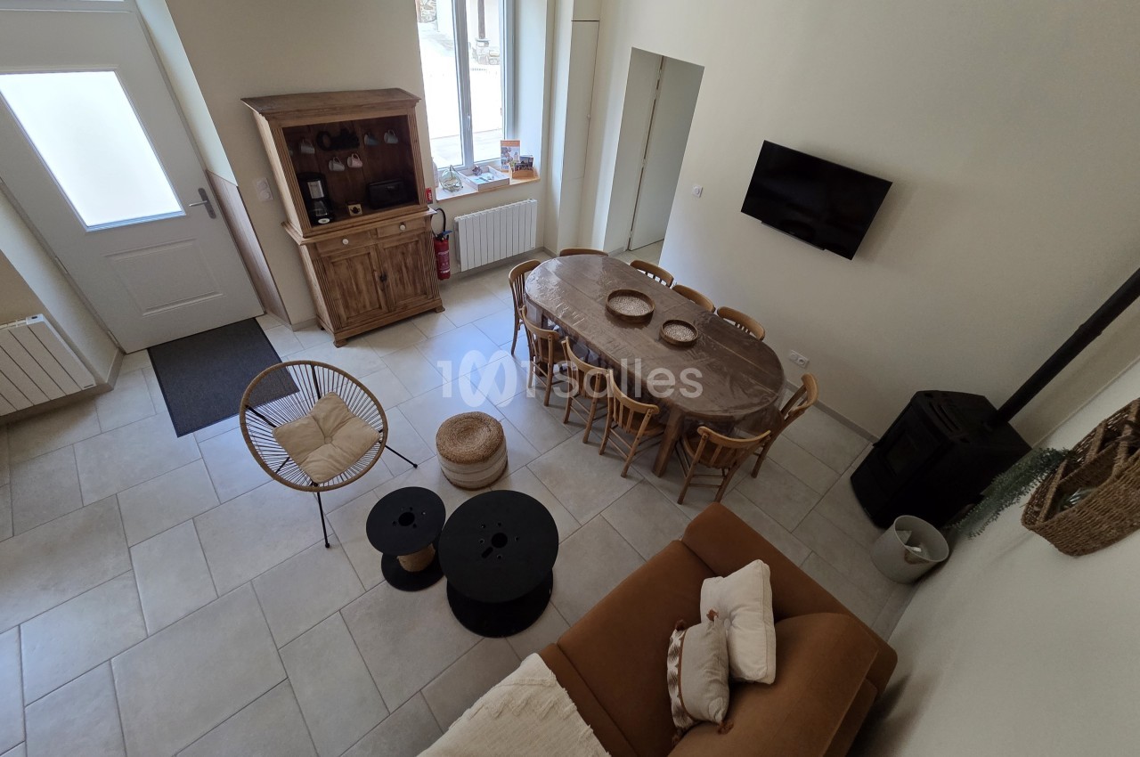 Vue d'une pièce de vie lumineuse avec table à manger, canapé, poêle à bois et mobilier en bois clair.