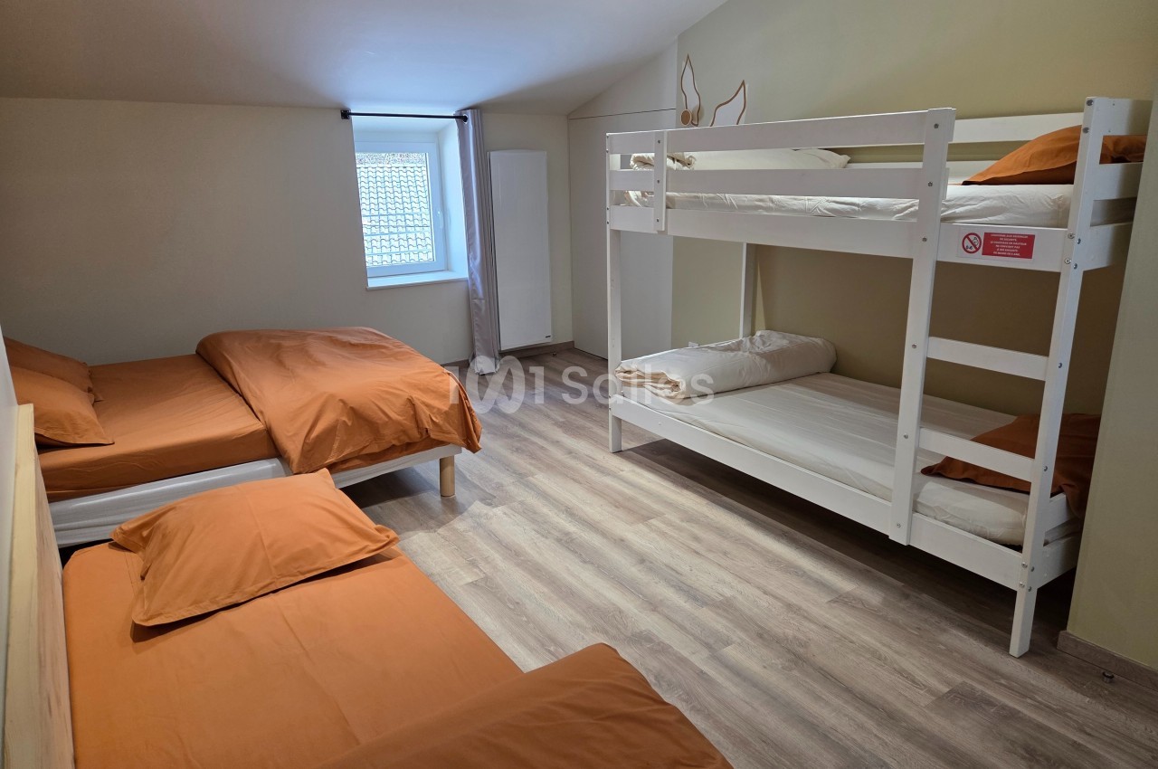 Chambre avec lits superposés et lits simples, draps orange, parquet clair et fenêtre avec lumière naturelle.