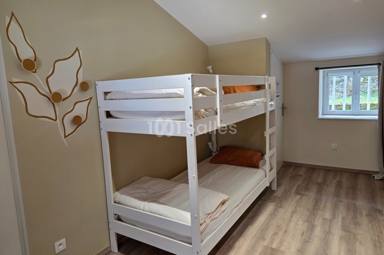 Lit superposé blanc dans une chambre lumineuse avec parquet, mur beige décoré et fenêtre donnant sur l'extérieur.
