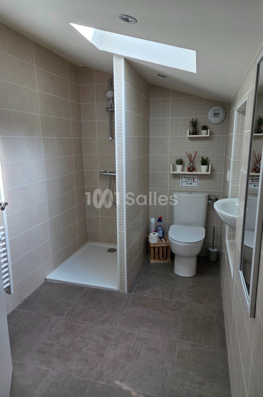 Salle de bain moderne avec douche à l'italienne, toilettes, lavabo, étagères murales et lumière naturelle.