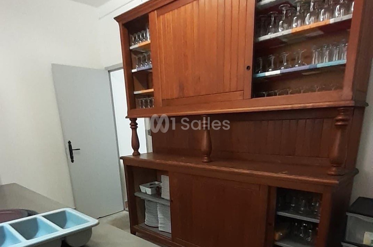 Buffet en bois avec portes vitrées contenant des verres, situé dans une pièce avec un évier et une porte blanche.