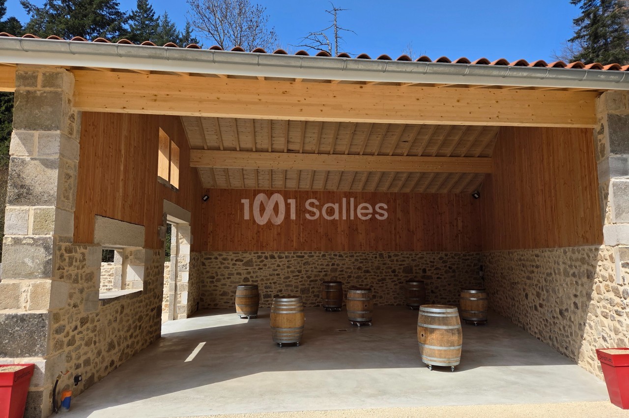 Salle ouverte avec murs en pierre et bois, contenant plusieurs tonneaux en bois sur roulettes, sous un ciel dégagé.
