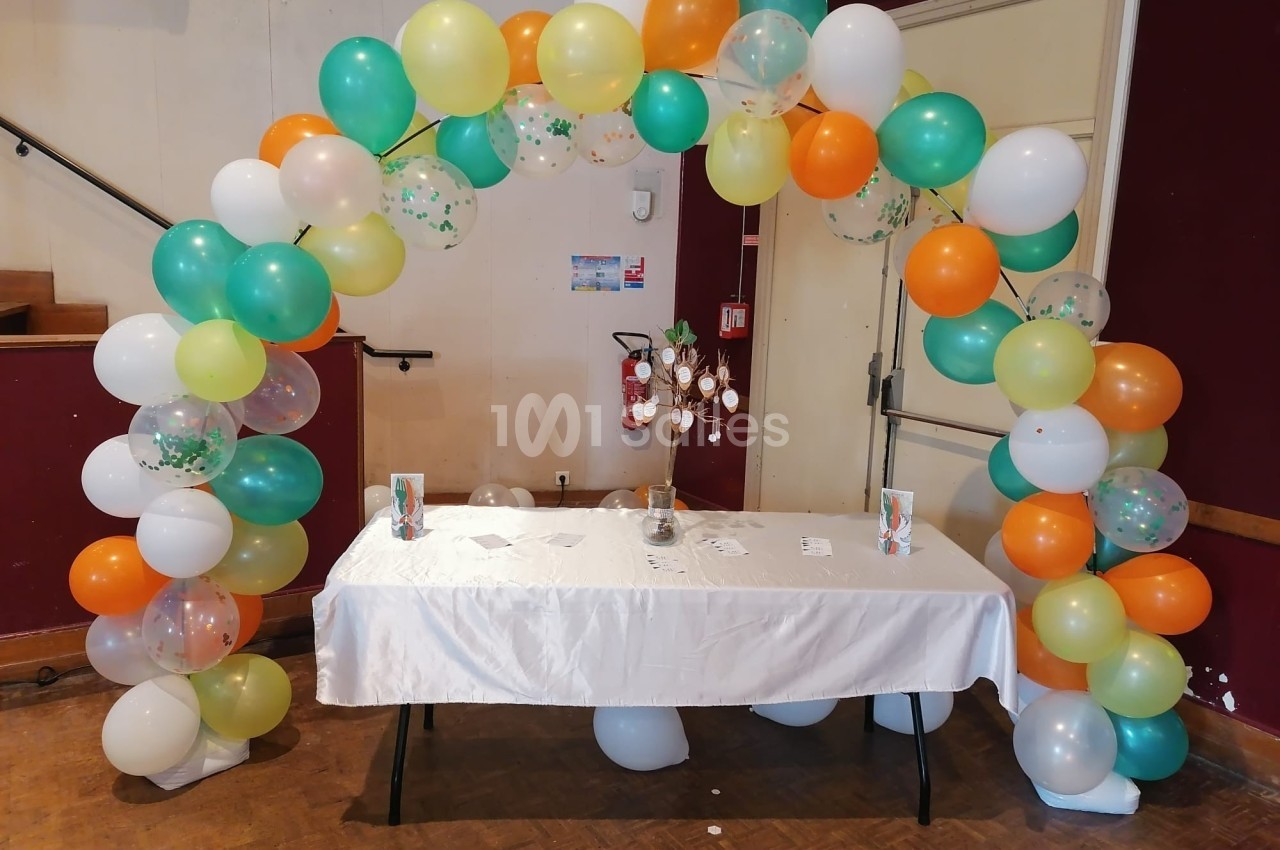 Arche de ballons colorés décorant une table recouverte d'une nappe blanche dans une salle intérieure.