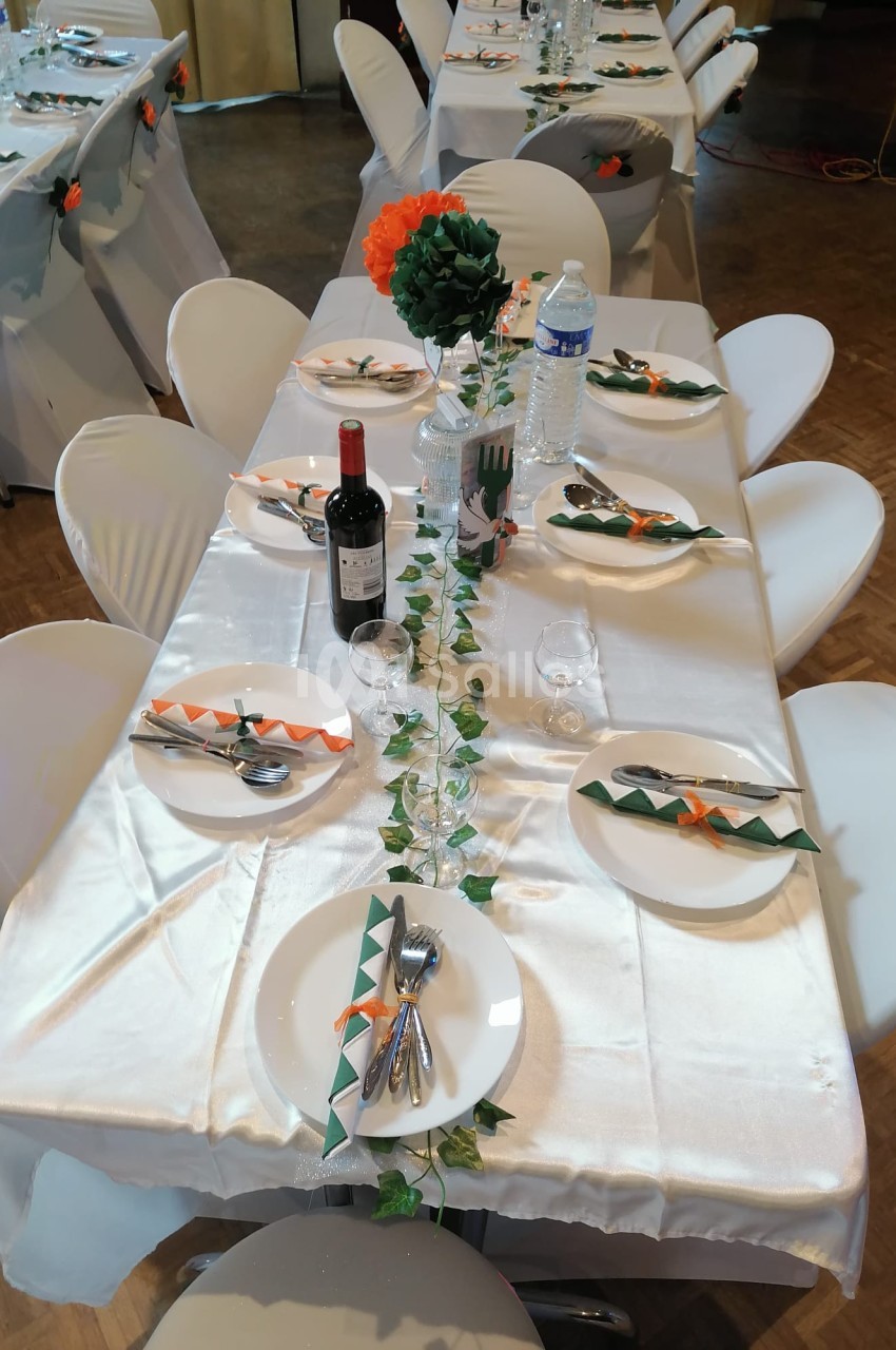 Table dressée avec une nappe blanche, décorée de serviettes vertes et orange, bouteilles, verres et centre de table floral.