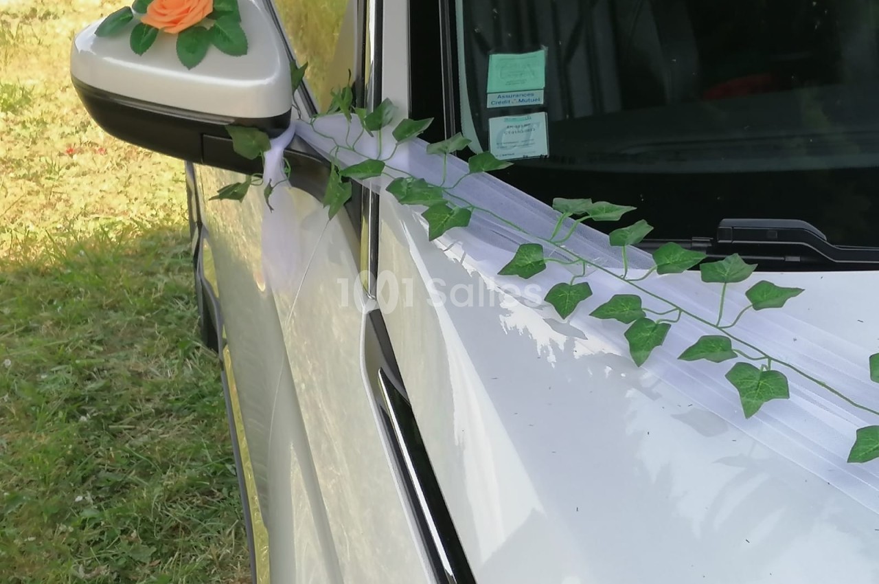 Décoration florale avec lierre et rose orange sur le rétroviseur d'une voiture blanche pour une cérémonie.