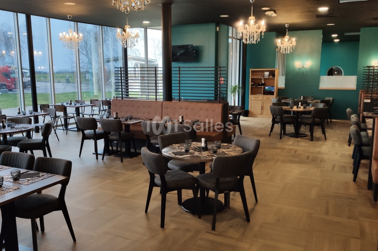Salle de restaurant moderne avec tables dressées, chaises rembourrées, banquettes et grandes baies vitrées donnant sur l…
