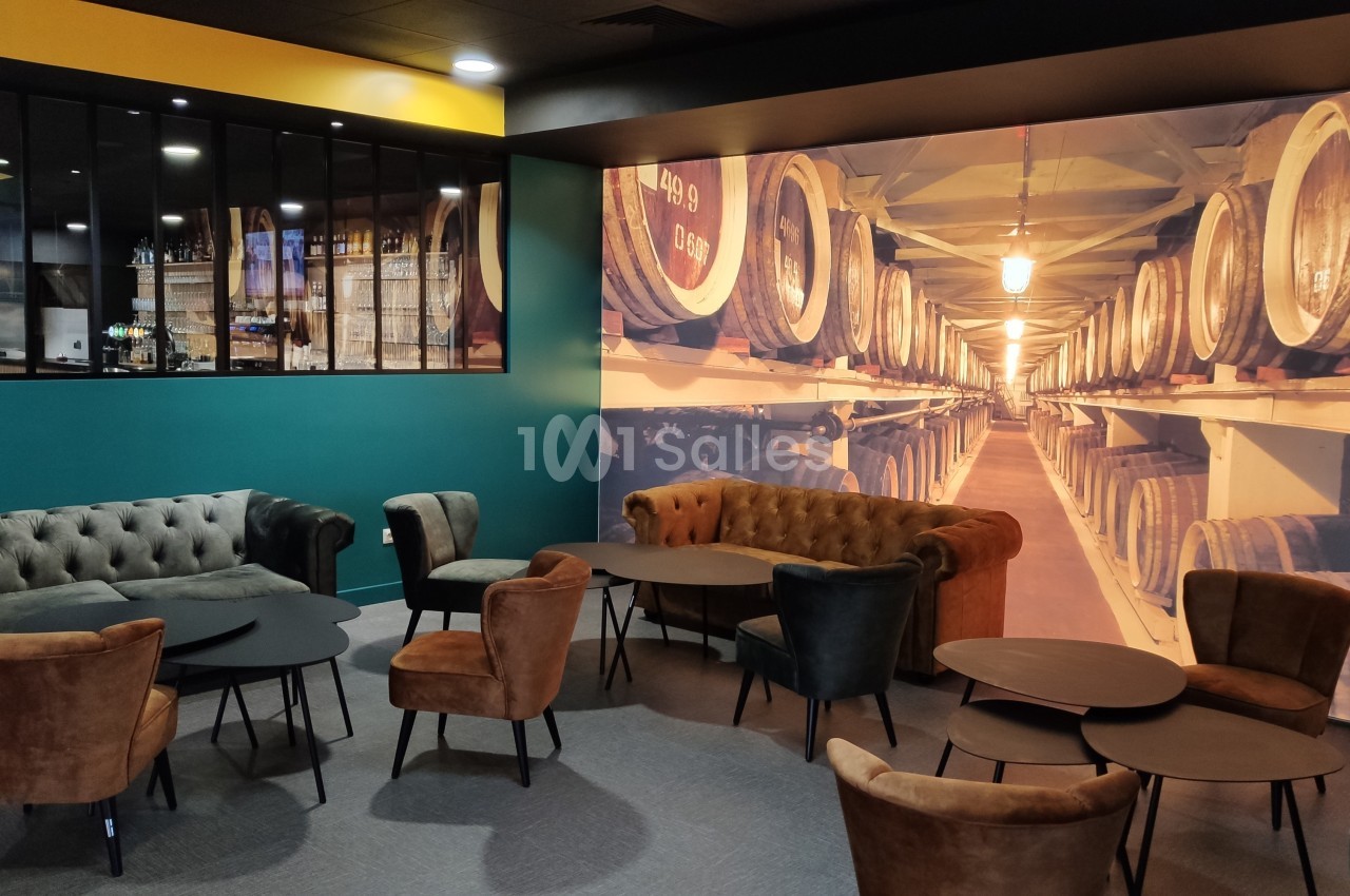 Espace lounge avec fauteuils et tables basses, décoré d'une grande photo de tonneaux dans une cave à vin.